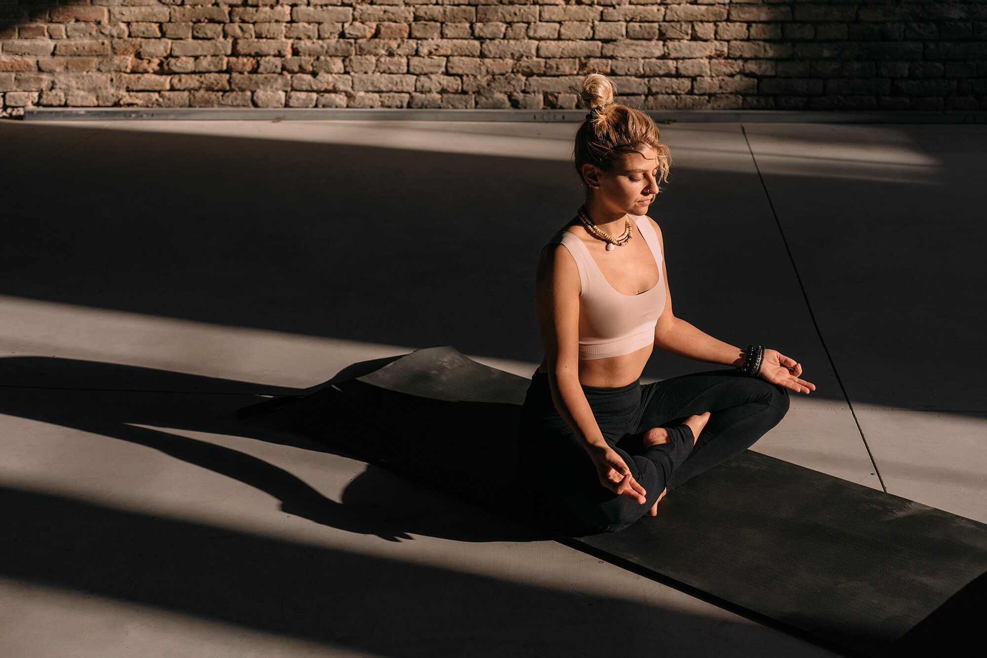 Woman meditating cross-legged in long afternoon shadows beside a brick wall