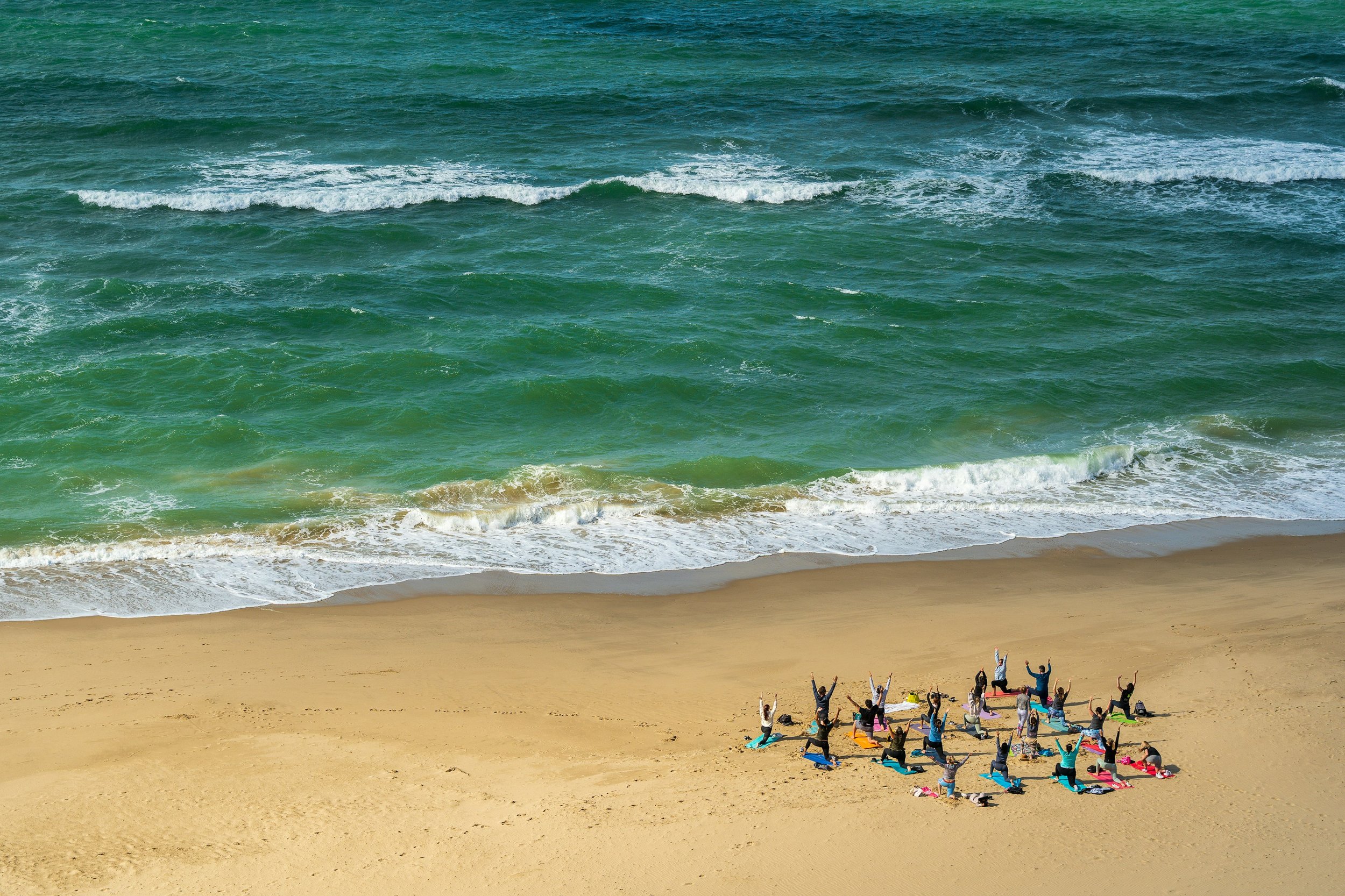Aerial view of a yoga class practising on the sand beside breaking surf