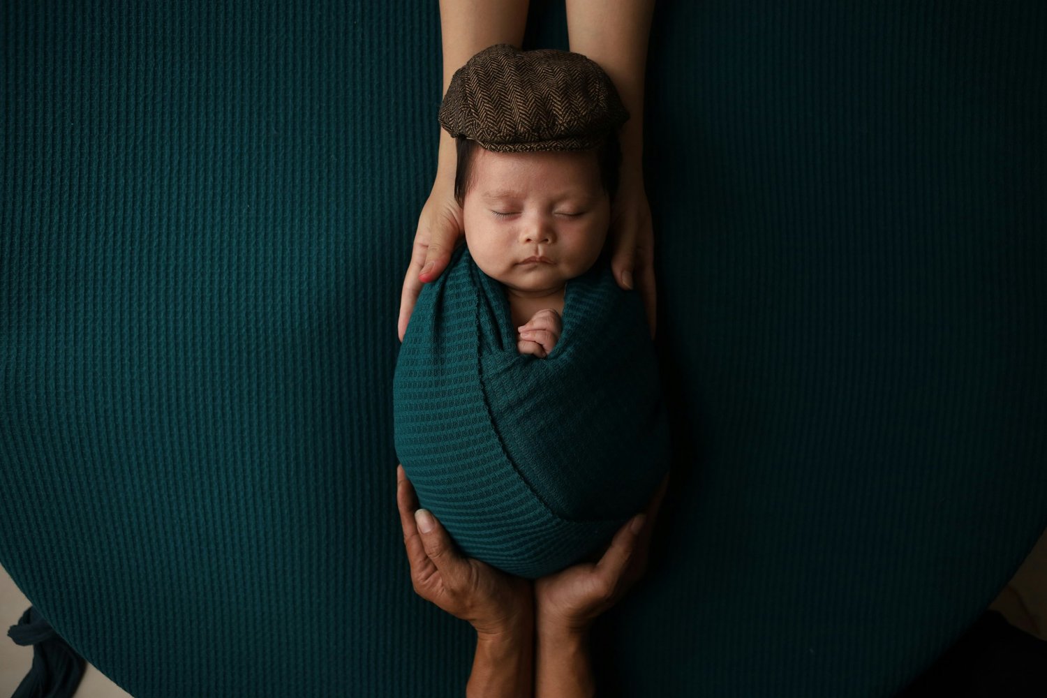 Newborn baby swaddled in dark green fabric, cradled in a parent's hands