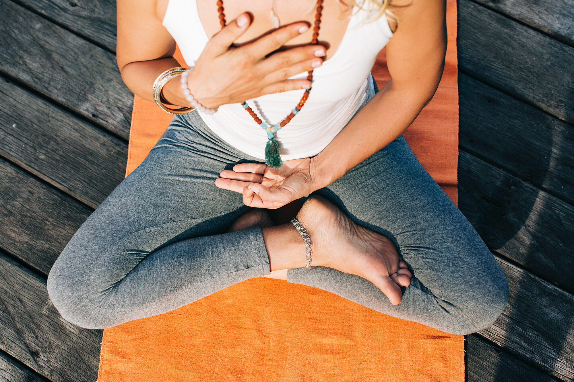 Practitioner seated cross-legged with mala beads resting in her lap on an orange mat