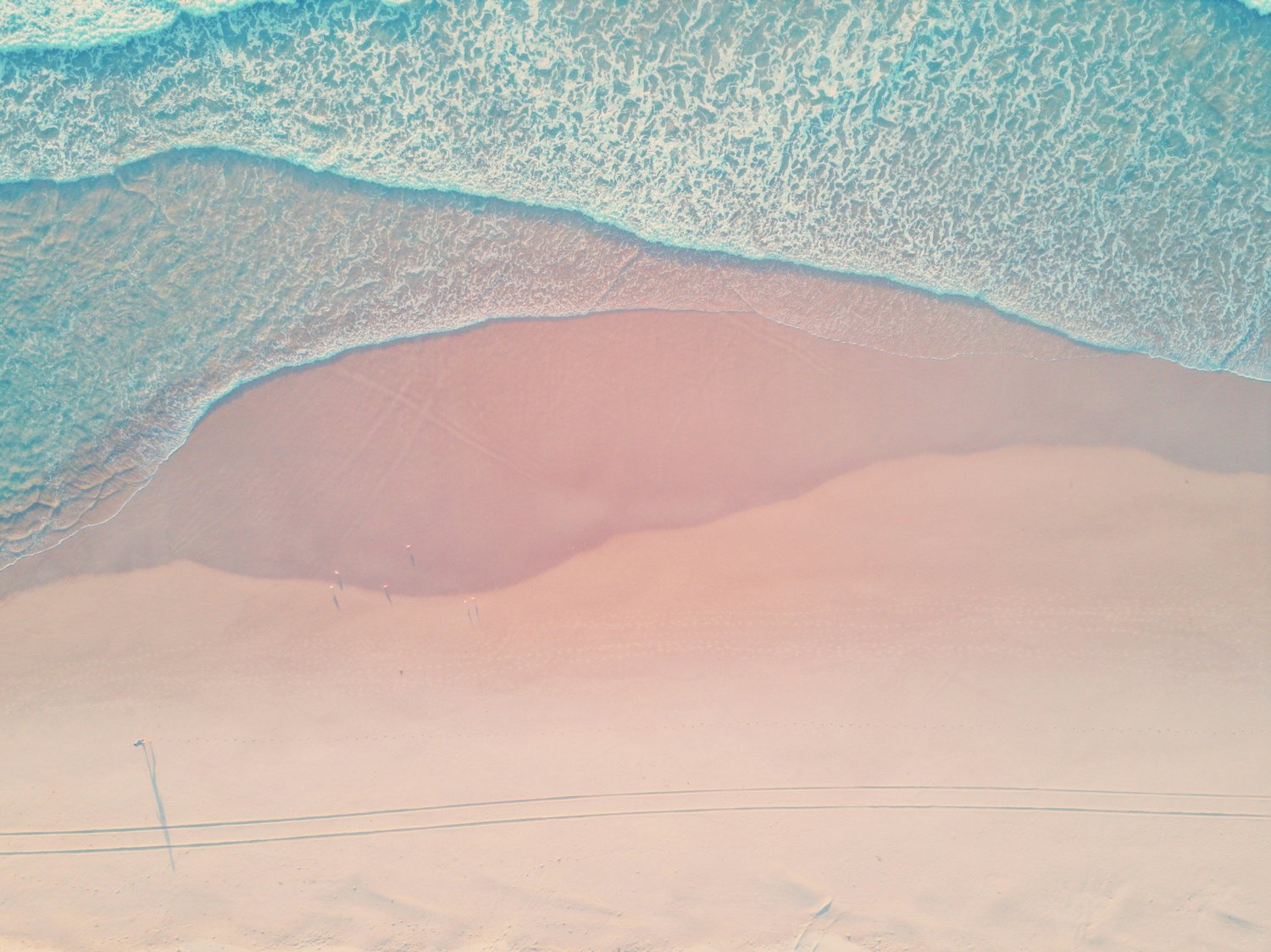 Aerial view of pale pink sand meeting turquoise shallows